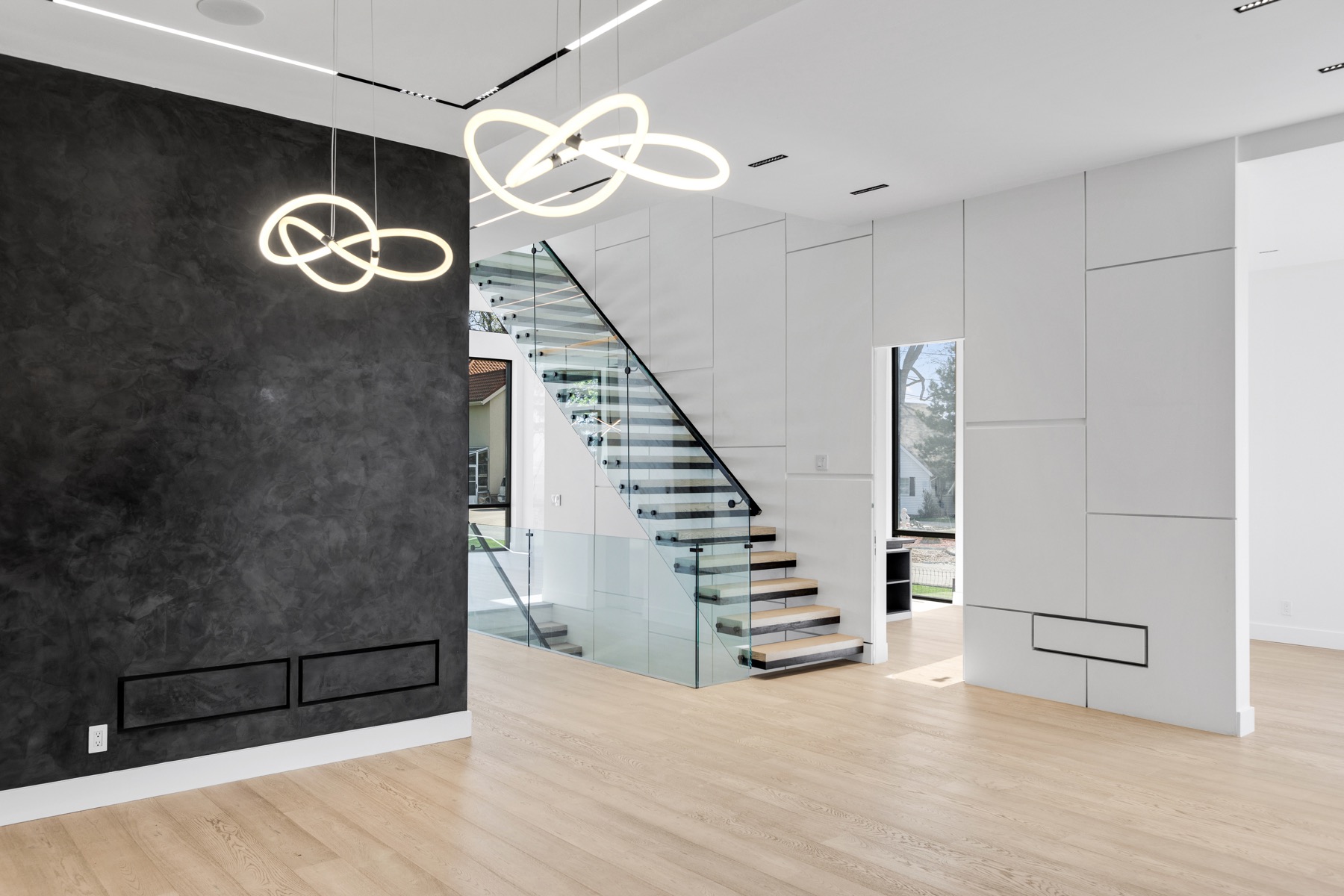 Sculptural pendants alongside linear ceiling lighting and a glass stair